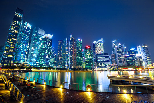 People enjoy the view of central business district from marina bay waterfront promenade in front of bayfront south jetty. Singapore cityscape illuminated by night.