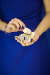 Beautiful woman in blue dress holding some shells in her hands. Close up picture at her hands, can be used as background - obrazy, fototapety, plakaty