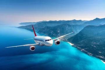 Poster Airplane is flying over islands and sea at sunrise in summer. Landscape with white passenger airplane, seashore, mountains, sky, and blue water. White passenger aircraft. Travel and resort. Tourism © den-belitsky