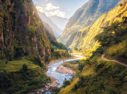 Colorful landscape with high Himalayan mountains, beautiful curving river, green forest, blue sky with clouds and yellow sunlight at sunset in summer in Nepal. Mountain valley. Travel in Himalayas