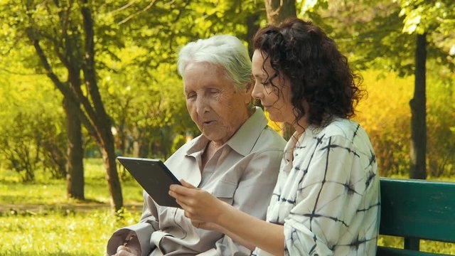 An elderly woman with granddaughter looks at photos on the tablet.
