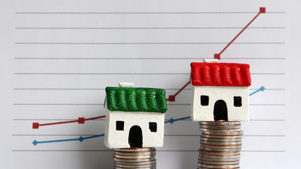 Housing price rising and differentiated concept. A miniature house on a pile of coins in front...