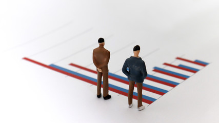 Fototapeta premium Appearance from behind of two miniature men standing on a bar graph.
