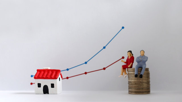 A miniature couple sitting on a pile of coins in front of a linear graph. The concept of increasing income gap.