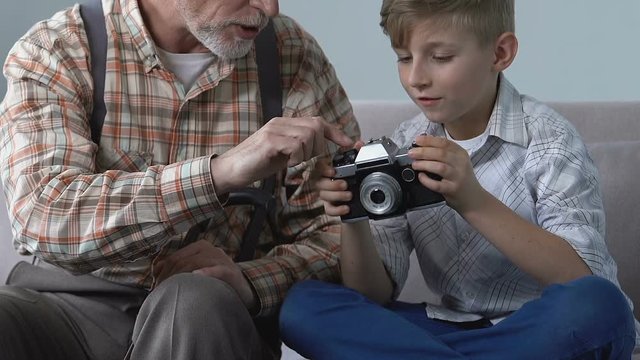Grandfather showing boy vintage photo camera, creative family hobby, leisure