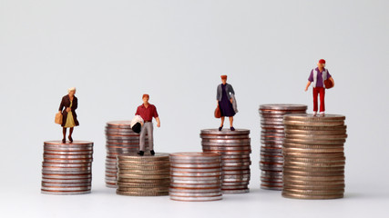 Miniature people standing on piles of different heights of coins. The growing concept of income gap.