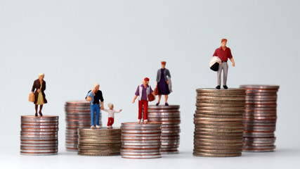 Miniature people standing on piles of different heights of coins. A concept of economic inequality.