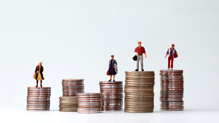 Miniature people standing on piles of different heights of coins. The concept of a growing income...