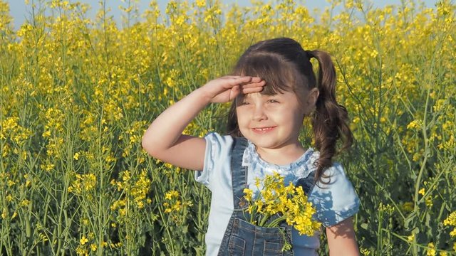 Child in a field of yellow flowers. A happy girl smelling canola flowers.