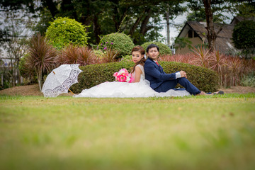 Beautiful Young wedding couple with white umbrellas sitting on a green lawn. Man gave flowers to...