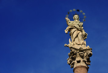 Fototapeta na wymiar Statue of Virgin Mary of the Stars crushing dragon and crescent at the top of an ancient column in the historic center of Lucca, erected in 1687 (with copy space)