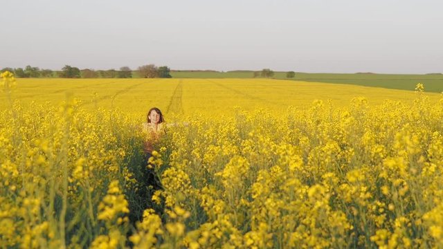 Child in a field of yellow flowers. A happy girl runs across the canola field.