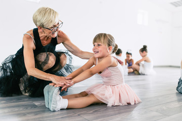 Charming senior ballet teacher learning little ballerina how to dance.