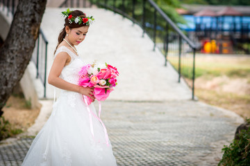 Woman wearing a wedding dress and with holding a bouquet of flowers standing on cement floor. Over...