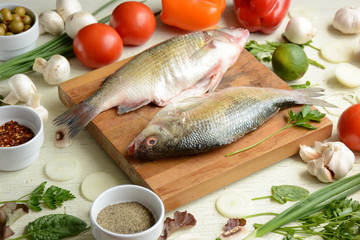 Fresh uncooked dorado or sea bream fish with lime, herbs,  vegetables and spices on rustic  wooden board over white backdrop, top view.   Healthy food or diet nutrition concept. 