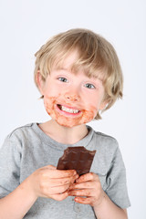 Young messy boy eating a chocolate bar with chocolate on his face and hands
