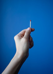 Woman hand holding match stick against blue background.