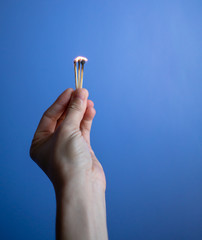 Woman hand holding burnt match stick against blue background.