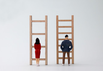 Miniature men and women standing in front of different ladders. The concept of discrimination of...