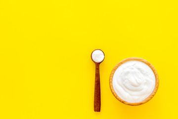 Healthy product, healthy meal. Greek yogurt in brown bowl near spoon on yellow background top view copy space