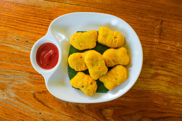 Fried chicken nuggets And tomato sauce on a white plate on a wooden table.
