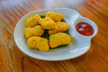 Fried chicken nuggets And tomato sauce on a white plate on a wooden table.