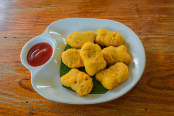 Fried chicken nuggets And tomato sauce on a white plate on a wooden table.