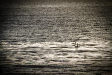 A sailboat at sea in the open ocean in the late afternoon.