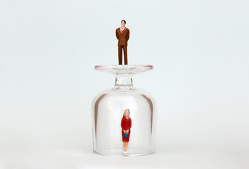 A miniature woman in a glass cup and a miniature man on top of a glass cup. The concept of the...
