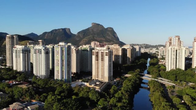 Aerial footage of Marapendi canal in Barra da Tijuca on a summer day, with slow rise to see Gavea Stone behind the tall residential skyscrapers