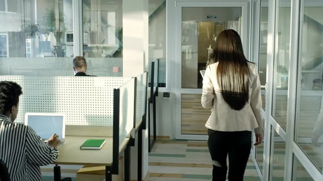 Tilt Up Rear View Of Businesswoman Walking With Documents Through Modern Open Space Office While Employees Working On Computers