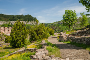 Fototapeta na wymiar Alleyway in the park on Tsarevets hill, Veliko Tarnovo, Bulgaria. Photo was taken at sunny spring day. Ruins of ancient castle on the foreground. Ancient stonewall on the background.