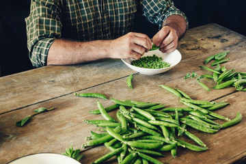Male hands clean green peas sitting wooden table kitchen Rustic style Green peas bowl wooden table