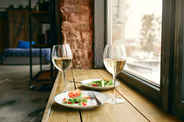 Two plates healthy vegetable salad glass white wine wooden window sill apartment