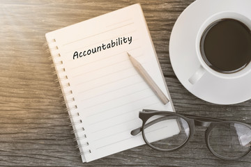 Accountability concept on notebook with glasses, pencil and coffee cup on wooden table. Business concept.