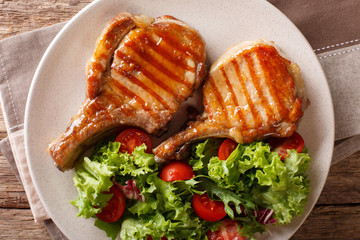 Delicious honey grilled chop pork served with a salad of fresh vegetables close-up on a plate. Horizontal top view