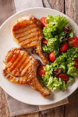 Delicious honey grilled chop pork served with a salad of fresh vegetables close-up on a plate. Vertical top view