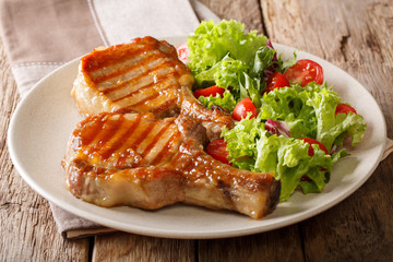 grilled pork steak with a bone in a sweet honey glaze and a salad of fresh vegetables close-up on a plate. horizontal