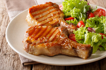 Barbecue food: a grilled pork chop in sweet honey glaze and a salad of fresh vegetables close-up on a plate on a table. horizontal