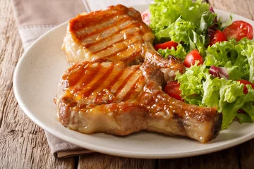 Fototapeten Barbecue food: a grilled pork chop in sweet honey glaze and a salad of fresh vegetables close-up on a plate on a table. horizontal © FomaA