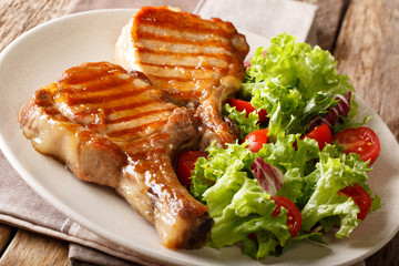 Delicious honey grilled chop pork served with a salad of fresh vegetables close-up on a plate. horizontal