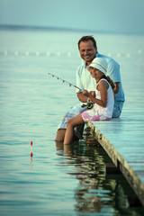 Father with his daughter fishing in a sea on a wood pier at sunset.