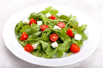 Salad with arugula, baby spinach, feta cheese and tomato cherry on white plate. Menu concept