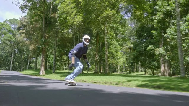 Front view follow shot of man in helmet enjoying skateboarding in green park on warm summer day
