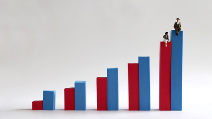 A miniature woman sitting on a red bar on a bar graph and a miniature man sitting on a blue bar. The concept of discrimination between men and women when employed by a company.