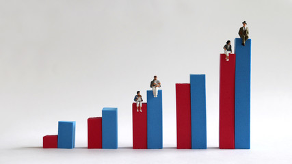 Two miniature women sitting on a red bar on a bar graph and two miniature men sitting on a blue...