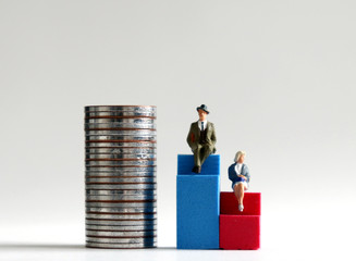 A miniature man sitting on a tall blue chair beside a pile of coins and a miniature woman sitting...