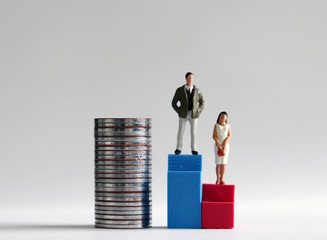 A miniature man standing on a tall blue stair beside a pile of coins and a miniature woman standing...