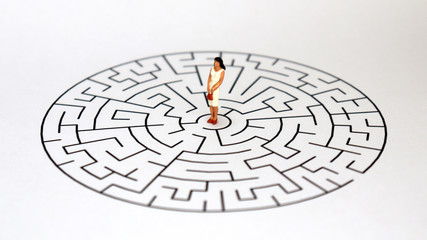 A maze and a miniature woman on a white background.
