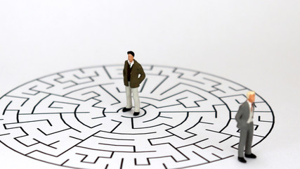 Miniature two men standing on a maze of white backgrounds.